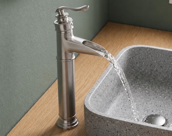 Op de afbeelding: Een eenhendelkraan van geborsteld nikkel met een gebogen uitloop die water in een rechthoekige grijze gespikkelde stenen waskom laat stromen. Het VINTROA-logo is rechtsboven zichtbaar. De kraan heeft een hoge cilindrische voet.