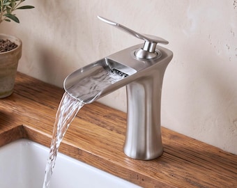 Op de afbeelding: Een badkamerkraan van geborsteld nikkel met een breed, open uitloopontwerp dat een watervaleffect creëert. De kraan is voorzien van een enkele hendel aan de bovenzijde voor waterregeling en toont het VINTROA-merklogo in de rechterbovenhoek.