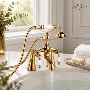 May include: A polished gold bathroom faucet with a handheld shower attachment, featuring white ceramic handles with black floral accents and the VINTROA logo. The faucet has a curved spout with water flowing into a white porcelain sink basin.