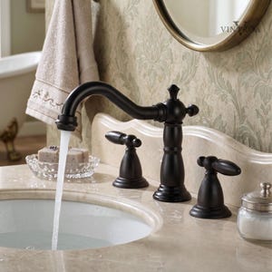 Puede incluir: Un grifo de baño de bronce oscuro con un caño curvo y tres manijas. El agua fluye del grifo a un lavabo blanco. El grifo está sobre una encimera de mármol y un papel pintado floral.
