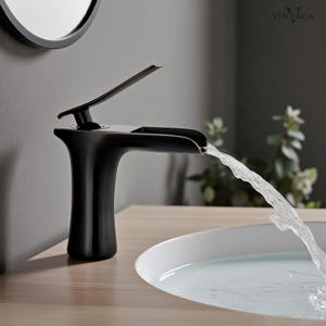 Può includere: Un moderno rubinetto da bagno nero con una maniglia color bronzo. L'acqua scorre dal rubinetto in un lavandino bianco. Il rubinetto è montato su una superficie di legno chiaro. Uno specchio rotondo è visibile sullo sfondo.