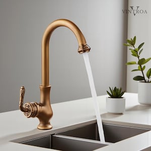 Puede incluir: Grifo de cocina de color bronce con un caño de arco alto, agua fluyendo y detalles decorativos. El grifo tiene un mango de palanca y está sobre un fondo neutro. La marca "VINTROA" es visible en la esquina superior derecha.