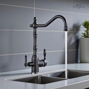 Puede incluir: Un grifo de cocina negro mate con un ca&ntilde;o de arco alto y dos manijas de palanca. El agua fluye desde el ca&ntilde;o hacia un fregadero doble de acero inoxidable. El grifo tiene un dise&ntilde;o decorativo y est&aacute; colocado contra una pared de azulejos gris.