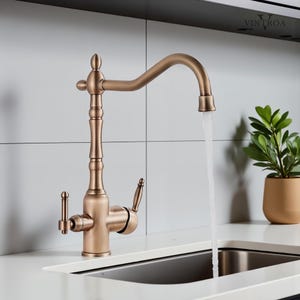 Puede incluir: Un grifo de cocina de color bronce con un ca&ntilde;o de arco alto y dos manijas de palanca. El agua fluye del ca&ntilde;o a un fregadero de acero inoxidable. El grifo tiene un dise&ntilde;o vintage y est&aacute; colocado contra una pared de azulejos blancos.
