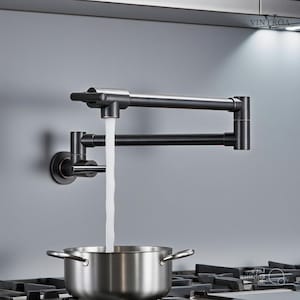 Puede incluir: Un grifo de llenado de ollas de bronce oscuro con agua que fluye hacia una olla de acero inoxidable sobre una estufa. El grifo está montado en la pared y tiene un brazo multiarticulado para un posicionamiento flexible. El grifo es de Vintroa.