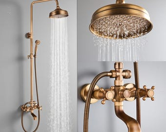 Op de afbeelding: Antieke messing douchekraan met een ronde douchekop en een handdouche. De douchekop bevindt zich boven de kraan en het water stroomt. De armatuur heeft een vintage design met kruisvormige handgrepen en een gebogen uitloop.