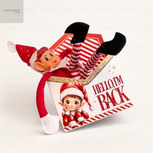 May include: A decorative paper envelope featuring red and white diagonal stripes and the text HELLO I'M BACK in red glitter. A plush elf doll with a red hat, red and white striped legs, and black boots is emerging from the top of the envelope.