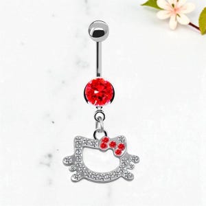 May include: A silver belly button ring featuring a red gem and a dangling charm. The charm is a cat's head shape, outlined with clear gems and a red gem bow.
