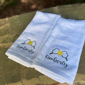 May include: Two white towels with embroidered yellow and green pickleball paddles and the name "Kimberly" in black cursive.