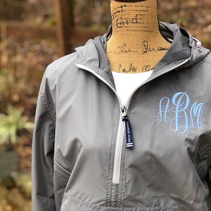 May include: A gray hooded jacket with a zipper closure and a white zipper pull. The jacket has a blue monogram on the front that says "ARM".