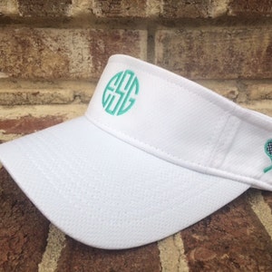 May include: White tennis visor with a green monogram "ESG" and two green tennis rackets with black and white checkered detail.