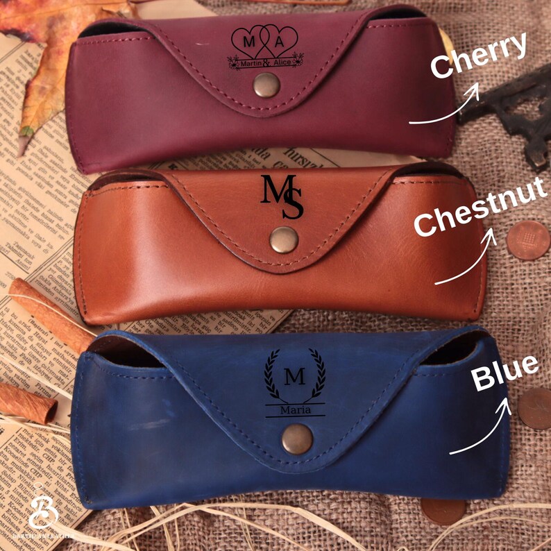Puede incluir: Tres estuches de cuero para gafas en color cereza, casta&ntilde;o y azul. Cada estuche tiene un cierre de bot&oacute;n a presi&oacute;n e iniciales o nombres personalizados. El estuche cereza tiene "Martin & Alice". El estuche casta&ntilde;o tiene "M". El estuche azul tiene "Maria".