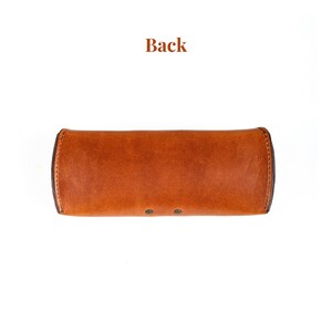 Puede incluir: Un estuche de gafas de cuero marr&oacute;n con forma rectangular redondeada. El estuche tiene una superficie texturizada y est&aacute; asegurado con dos peque&ntilde;os remaches. La palabra "Back" est&aacute; impresa en la parte superior de la imagen.