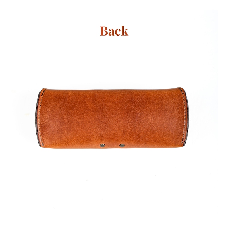 Puede incluir: Un estuche de gafas de cuero marr&oacute;n con forma rectangular redondeada. El estuche tiene una superficie texturizada y est&aacute; asegurado con dos peque&ntilde;os remaches. La palabra "Back" est&aacute; impresa en la parte superior de la imagen.