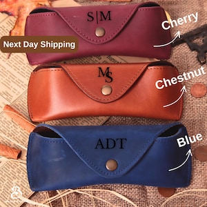 May include: Three leather eyeglass cases in cherry, chestnut, and blue. Each case has a snap closure and personalized initials. The cherry case has "S|M", the chestnut case has "M", and the blue case has "ADT".
