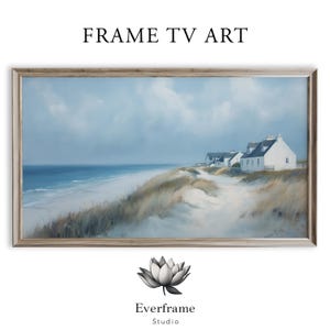 Puede incluir: Pintura de paisaje enmarcada de una escena costera con edificios blancos, una playa de arena y océano bajo un cielo nublado. La obra de arte está etiquetada como "FRAME TV ART" y "Everframe Studio".