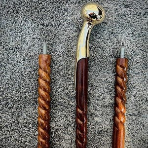 Puede incluir: Un bastón desmontado en tres segmentos. El segmento superior presenta un mango de metal dorado pulido con un cuello curvo. Los dos segmentos inferiores están hechos de madera marrón oscura con una textura retorcida y conectores metálicos roscados.
