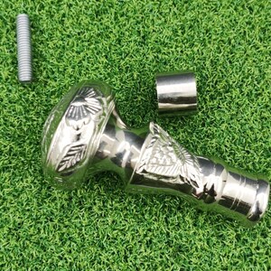 May include: A silver-colored cane handle with floral and bird-like designs. The handle is accompanied by a silver metal cylinder and a silver screw. The items are displayed on a green surface.