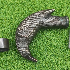 May include: A bronze-colored cane handle shaped like a bird's head, with detailed feather carvings. Includes a metal collar and a silver screw. The handle is approximately 6 inches long.