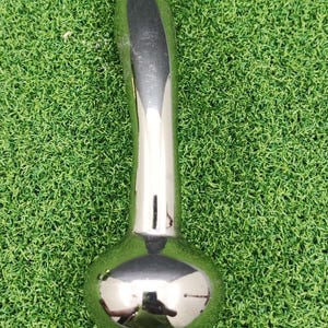 May include: A shiny, chrome-finished metal object with a bulbous base and a curved handle. The surface reflects the surroundings. The item is set against a backdrop of green artificial turf.