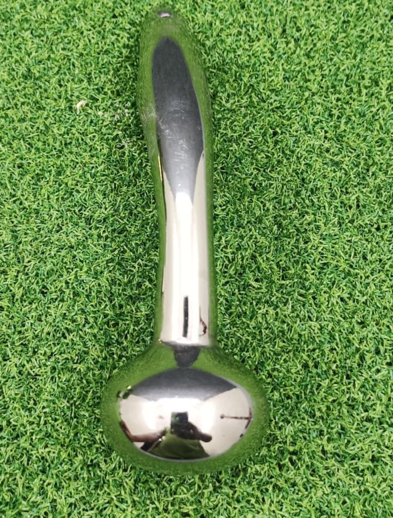 May include: A shiny, chrome-finished metal object with a bulbous base and a curved handle. The surface reflects the surroundings. The item is set against a backdrop of green artificial turf.