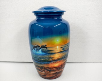 Puede incluir: Una urna funeraria azul con un acabado brillante. La urna presenta una imagen escénica de delfines saltando de las olas del océano al atardecer. La urna tiene una tapa a juego y está diseñada para contener las cenizas de un ser querido.