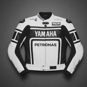 May include: A white and black Yamaha motorcycle racing jacket. The jacket features the Yamaha logo, the Petronas logo, and the Yamalube logo. The jacket has black accents on the sleeves and shoulders. The jacket has a zipper closure and a small buckle at the waist.