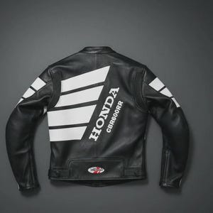 May include: Black leather motorcycle jacket with white Honda logo and CBR600RR text on the back. White stripes accent the shoulders and upper back. The jacket has a classic biker style with a tailored fit.