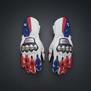 May include: Pair of white motorcycle gloves with red, blue, and silver detailing. The gloves display the BMW logo and the word "Motorrad". They have protective knuckle armour.