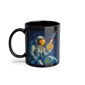 May include: Black ceramic mug featuring an astronaut holding a Bitcoin coin in space, with a rocket launching in the background. The design includes the Earth and a starry sky, with vibrant colors and detailed illustrations.