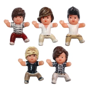 May include: Five small plastic figurines of young men in various outfits. One wears a striped top and red trousers, while others sport white or black shirts with khaki or beige trousers. Each figure has a different hairstyle.