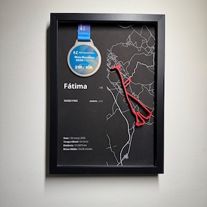 May include: A black framed display featuring a silver medal with a blue ribbon, a red 3D race route map, and white text including Fátima, Hugo Pais, and race statistics like 21,0975 km, 01:34:31 time, and 04:28 min/km pace on a black background.