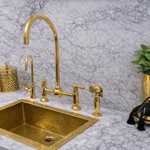 May include: A kitchen sink with a gold faucet, sprayer, and hammered copper sink. A gold container with a yellow tassel and a black and gold decorative piece are on the countertop. A gold planter holds a green plant.