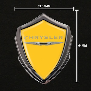Puede incluir: Un emblema Chrysler amarillo y plateado, en forma de escudo, con el nombre de la marca en letras plateadas. El emblema mide 5,33 cm de ancho y 6,4 cm de alto. El emblema tiene un borde plateado y un centro amarillo.
