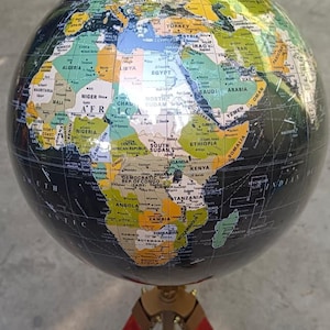 Könnte beinhalten: Ein detaillierter Globus mit schwarzer Basis und farbenfrohen Kontinenten, montiert auf einem Stativ mit roten und goldenen Akzenten. Der Globus zeigt Ländernamen und geografische Details, ideal für Bildungszwecke oder Dekoration.