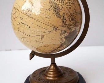Op de afbeelding: Een globe in vintage-stijl met een crèmekleurige kaart en bronzen metalen accenten. De globe is gemonteerd op een donkere houten voet met een bronzen metalen standaard. De globe is een decoratief item.