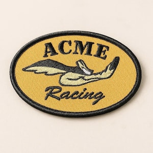 May include: Oval-shaped embroidered patch with a yellow background and black border. The patch features the words "ACME Racing" in black, with a stylized cartoon bird in the center. The patch is likely for clothing or accessories.