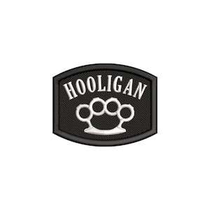 May include: A black embroidered patch with a curved top and bottom edge. The patch features the white text HOOLIGAN arched over a white graphic of brass knuckles. The design is enclosed by a thick black border with a visible stitched texture.