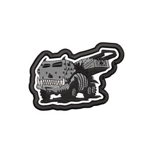 May include: Embroidered patch featuring a stylized, cartoonish monster truck with a menacing grin and studded details. The design is primarily gray and black, with a thick black border. The truck has large wheels and a detailed, textured appearance.