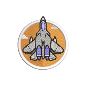 Op de afbeelding: Geborduurde patch met een gestileerde grijze straaljager met paarse accenten, tegen een oranje achtergrond. Het ontwerp bevat witte wolken en wordt omlijst door een witte cirkelvormige rand.