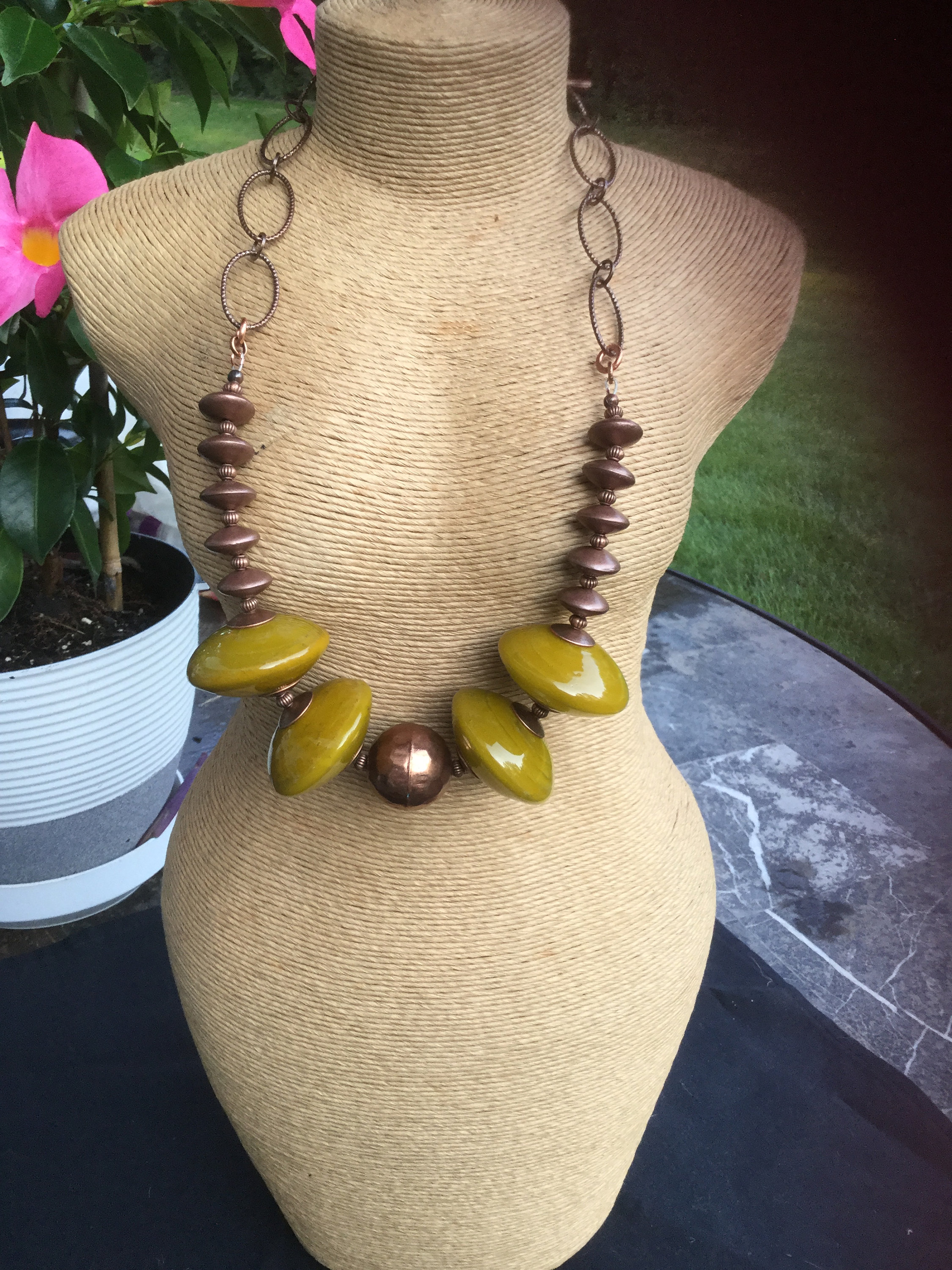 May include: A long necklace with a copper chain and large, green, round beads. The necklace is displayed on a brown mannequin.