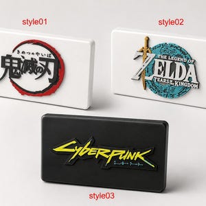 May include: Three rectangular plaques featuring video game and anime logos. Style01 is white with a Demon Slayer logo. Style02 is white with The Legend of Zelda: Tears of the Kingdom logo. Style03 is black with a yellow Cyberpunk 2077 logo.