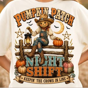 May include: A cream-colored t-shirt featuring a graphic of a scarecrow sitting on a wooden fence, holding a lantern. The text reads PUMPKIN PATCH NIGHT SHIFT KEEPIN THE CROWS IN LINE, surrounded by pumpkins, stars, a crescent moon, and bats.