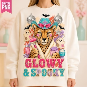 May include: A cream-colored sweatshirt featuring a graphic of a cheetah wearing a teal cowboy hat, a white robe, and holding a pink facial roller. The design includes disco balls, ghosts, skincare bottles, and the text GLOWY & SPOOKY in pink and teal.