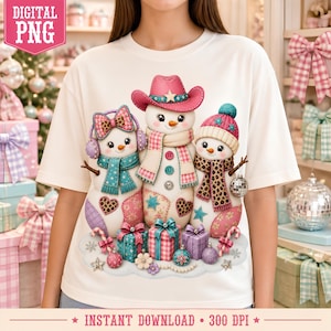 May include: A white t-shirt featuring a graphic of three snowmen wearing winter accessories including a pink cowboy hat, earmuffs, and scarves with leopard print and star patterns. The design includes colorful gift boxes and Christmas ornaments.