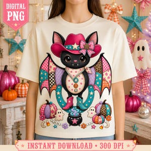 Puede incluir: Una camiseta color crema con el gráfico de un murciélago negro que lleva un sombrero de vaquero y botas rosas. El murciélago tiene alas estilo patchwork con estrellas y estampado de leopardo, un pañuelo y botones en el pecho, junto a calabazas.