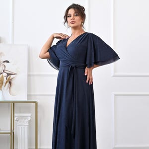May include: A navy blue wrap dress with a V-neck and short, flowing sleeves. The dress has a tie at the waist and a floor-length skirt. The fabric has a subtle shimmer. The dress is suitable for evening wear or special occasions.