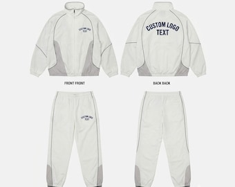 Può includere: Una tuta bianca e grigio chiaro composta da una giacca con zip e pantaloni abbinati. La giacca presenta un colletto alto e la scritta blu scuro CUSTOM LOGO TEXT sul petto e sulla schiena. I pantaloni riportano la scritta sulla coscia.