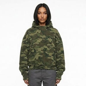 May include: A green camouflage hoodie with a front pocket and a high collar. The hoodie has a relaxed fit and is made of a soft material. The camouflage pattern features shades of green, brown, and black.