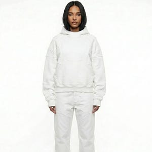 May include: A white hoodie with a matching pair of white pants. The hoodie has a front pocket and stitched detailing. The model is wearing a white outfit against a white background.